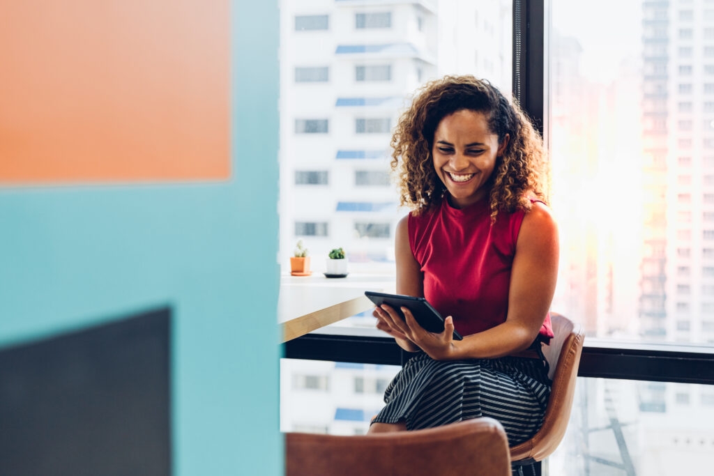 smiling business owner sitting at large window holding a tablet